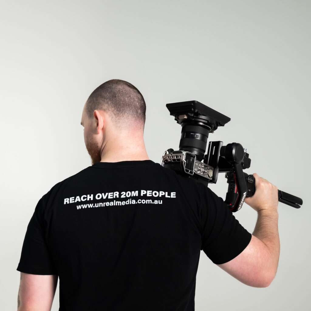 Videographer holding camera wearing branded shirt
