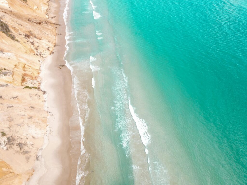 Drone view of turquoise waves on a Sunshine Coast beach beside sandstone cliffs, cinematic backdrop for brand videos.